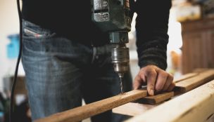 Close-up of a person using an electric drill on a wooden plank, showcasing detailed woodworking skills.